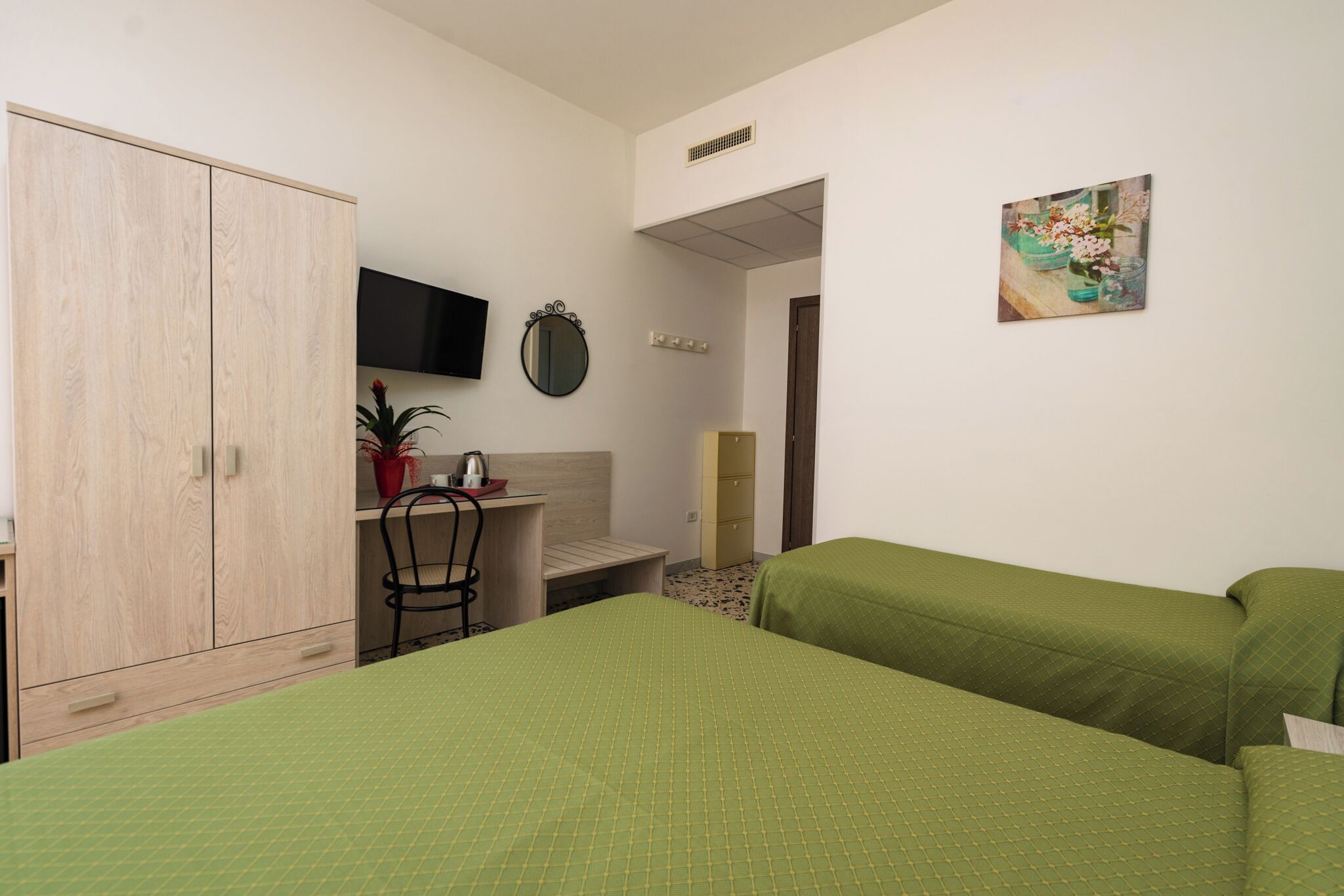 Una habitación con dos camas, un escritorio, una silla, un armario, un televisor y un cuadro en la pared.