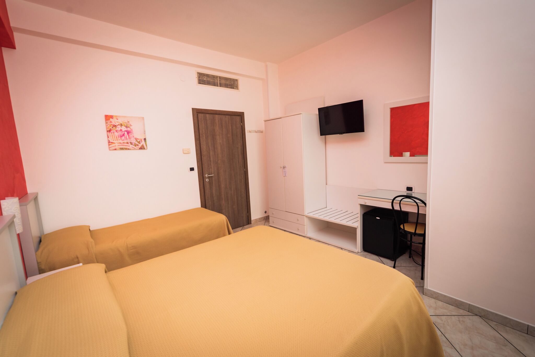 A room with two beds, a wardrobe, a desk, a chair, and a TV.