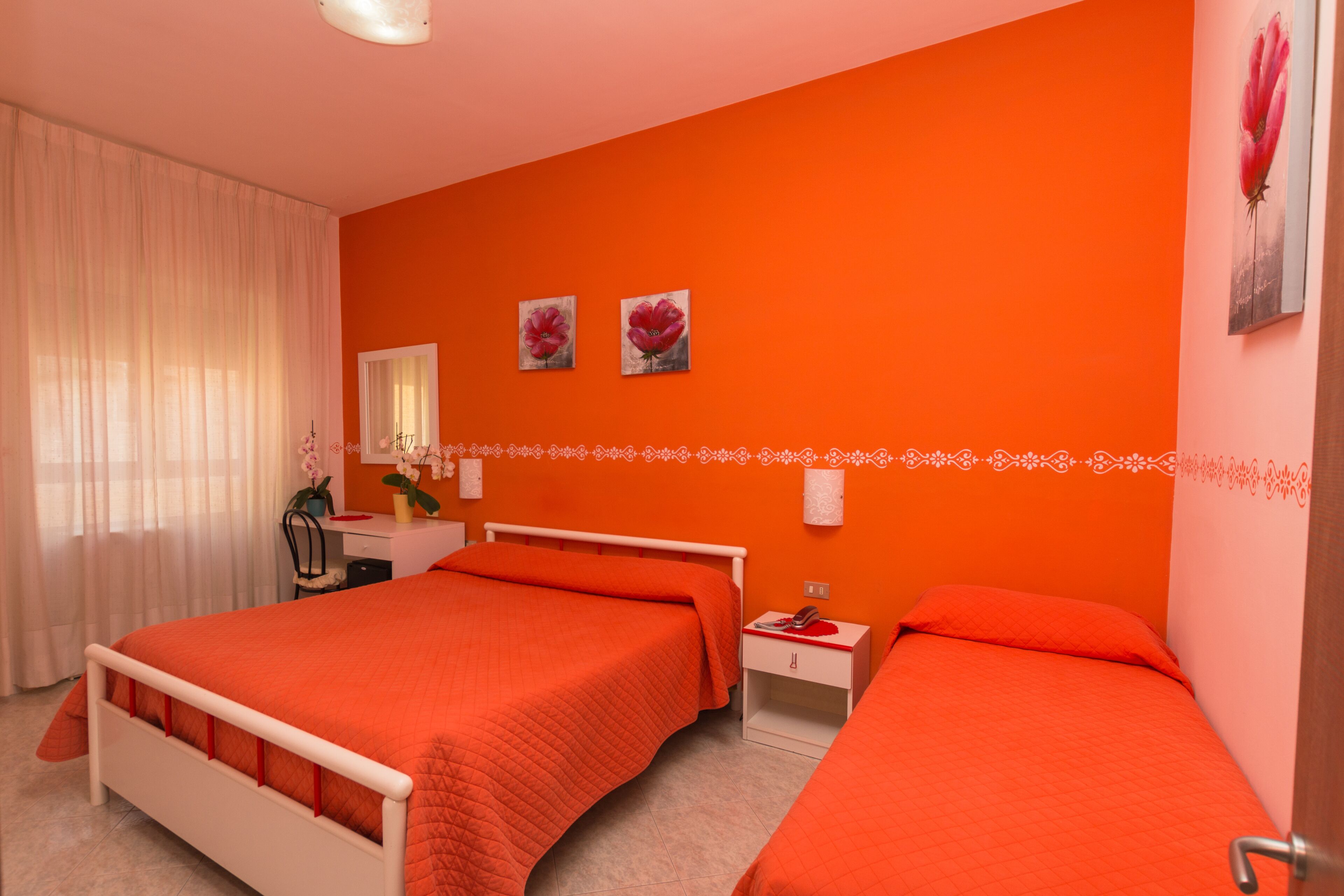 A hotel room with two beds, a desk, a chair, and a window with curtains.
