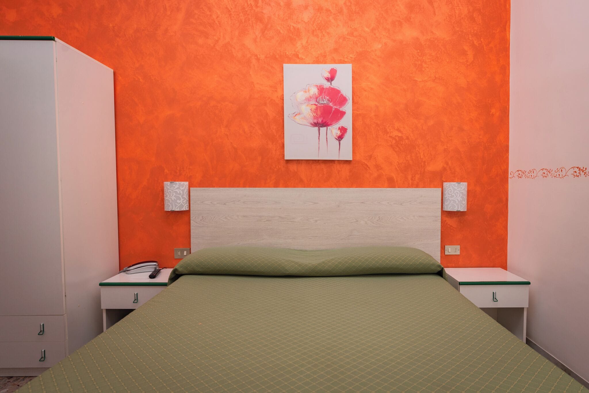 A bedroom with an orange wall, a wooden headboard, a green bedspread, and bedside tables with lamps.