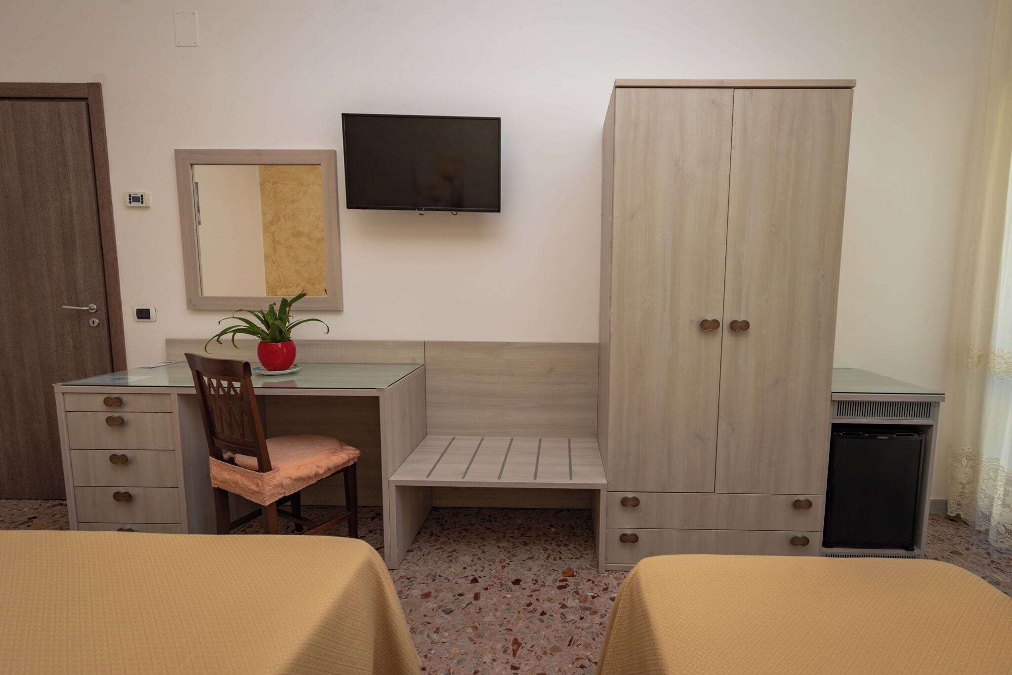 Une chambre d’hôtel équipée d’un bureau, d’une chaise, d’une armoire, d’une télévision et de deux lits.