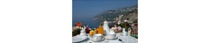 A table set with white dishes and a view of the sea and a mountainous landscape. - Baia Verde (Maiori)