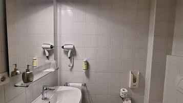 A bathroom with a sink, mirror, toilet, and a shelf with toiletries.