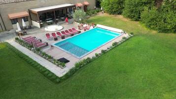 Una piscina con lettini, una veranda coperta e un prato curato.