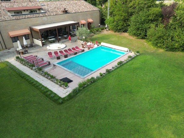 Una piscina con sillas de descanso, un patio cubierto y un césped cuidado.