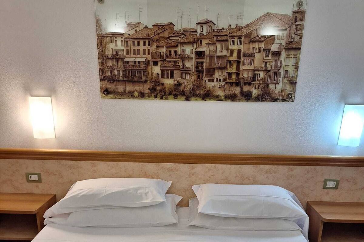 Une chambre d’hôtel avec un grand lit, deux tables de chevet et un tableau représentant une vue de la ville, accroché au mur.