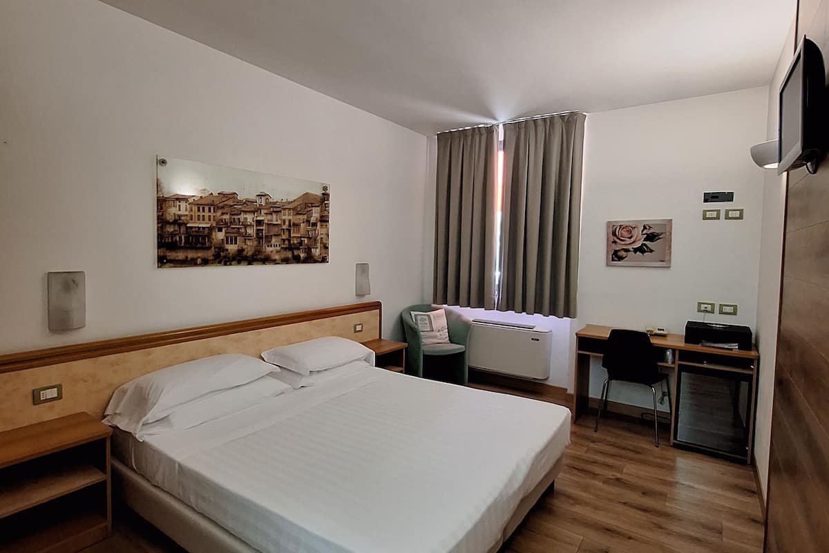 Une chambre d’hôtel avec un grand lit, un bureau, une chaise, un téléviseur à écran plat et une fenêtre avec des rideaux.