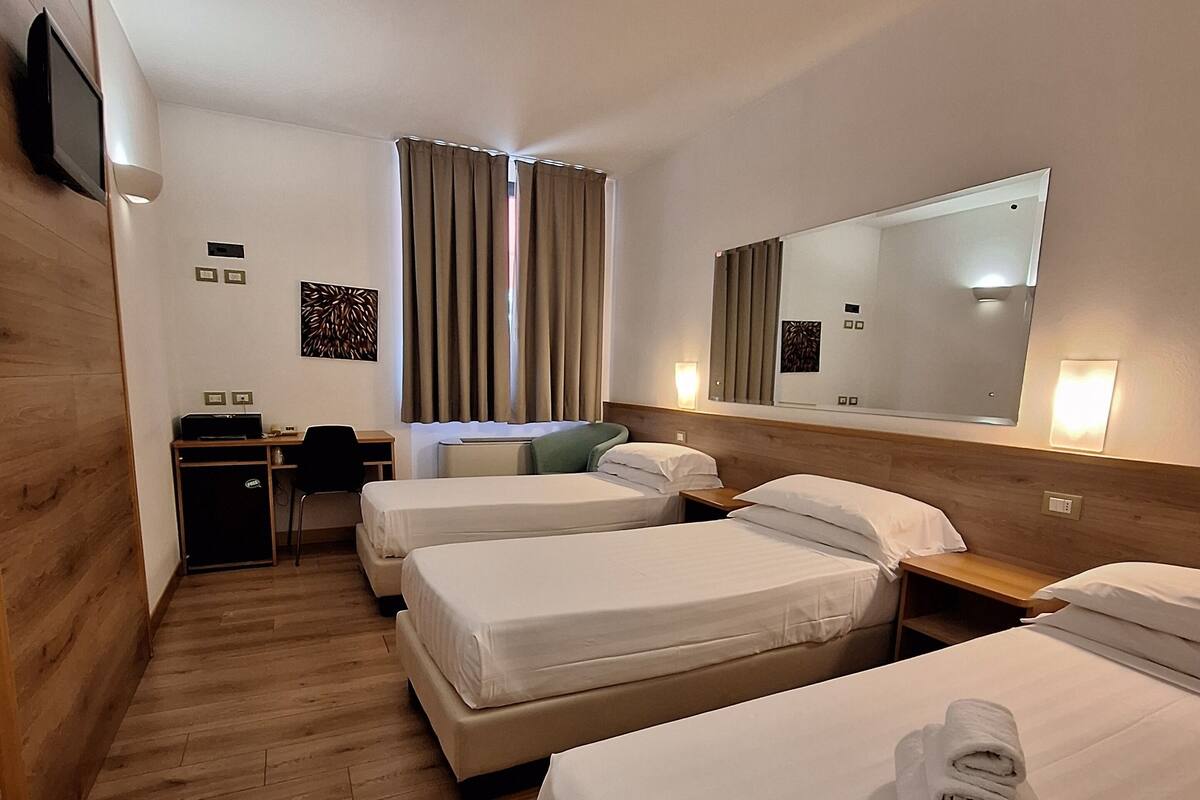 Une chambre d’hôtel avec trois lits, un bureau, une chaise et un téléviseur.