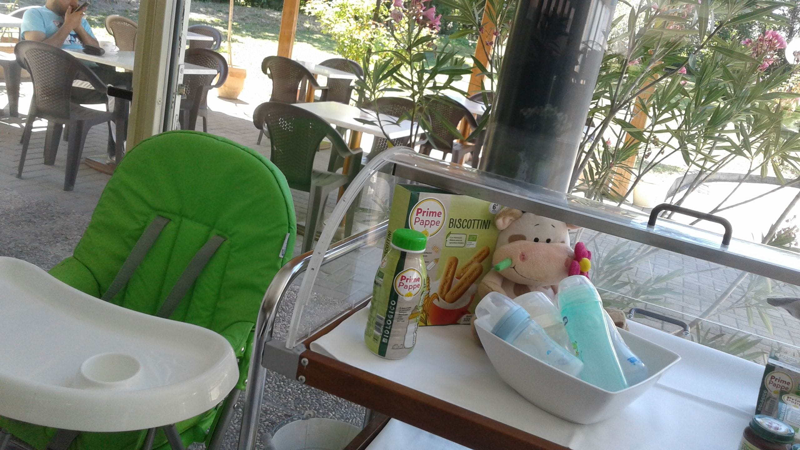 Zona pranzo con posti a sedere all'aperto, una sedia verde, un tavolo con una bottiglia di Prime Pappe, una scatola di biscotti e un peluche.