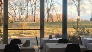 An outdoor dining area with tables and chairs, a view of a park with trees and grass, and a clear sky.