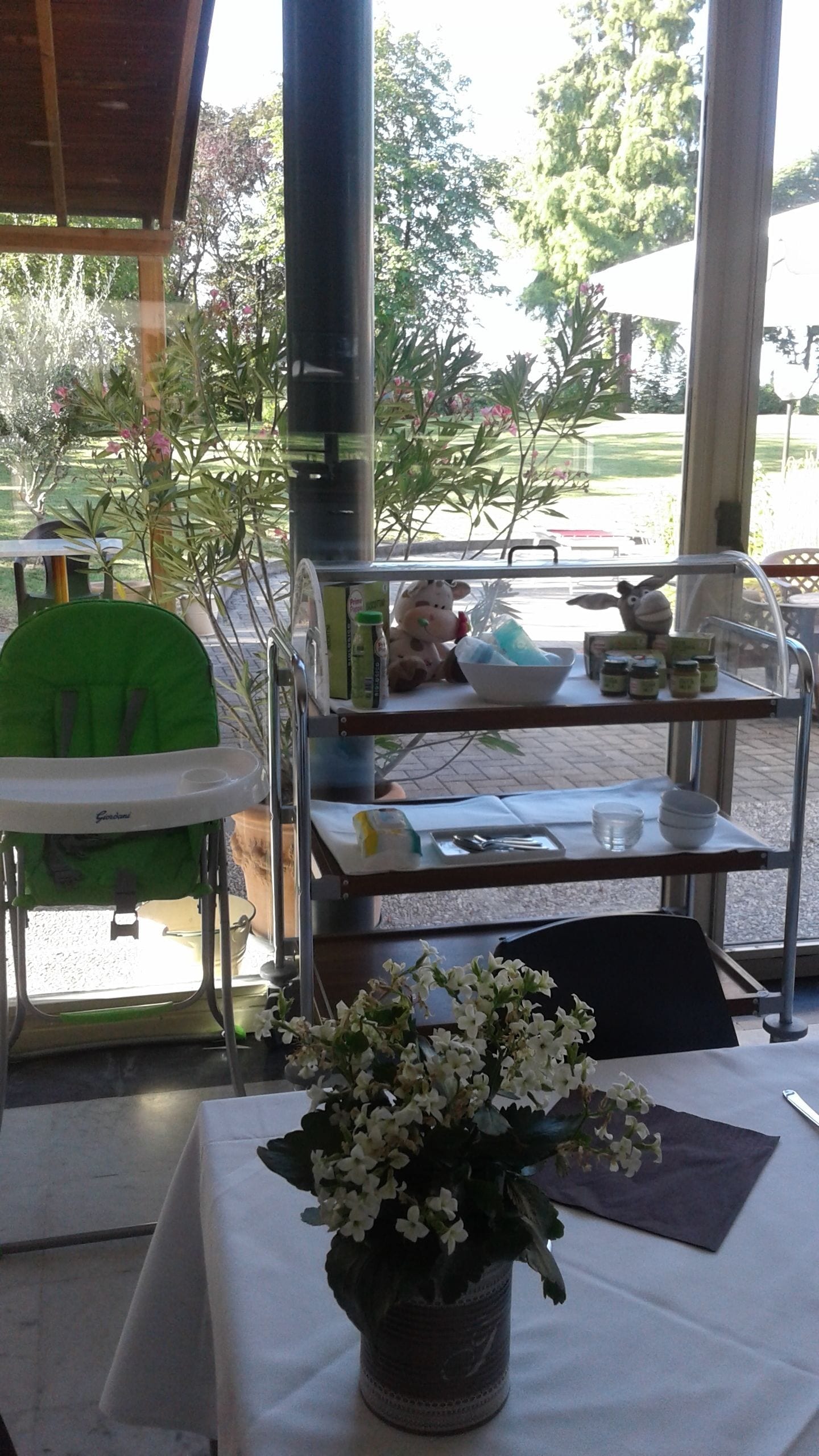 Un comedor con una mesa preparada para dos personas, una trona verde y un carrito con alimentos.