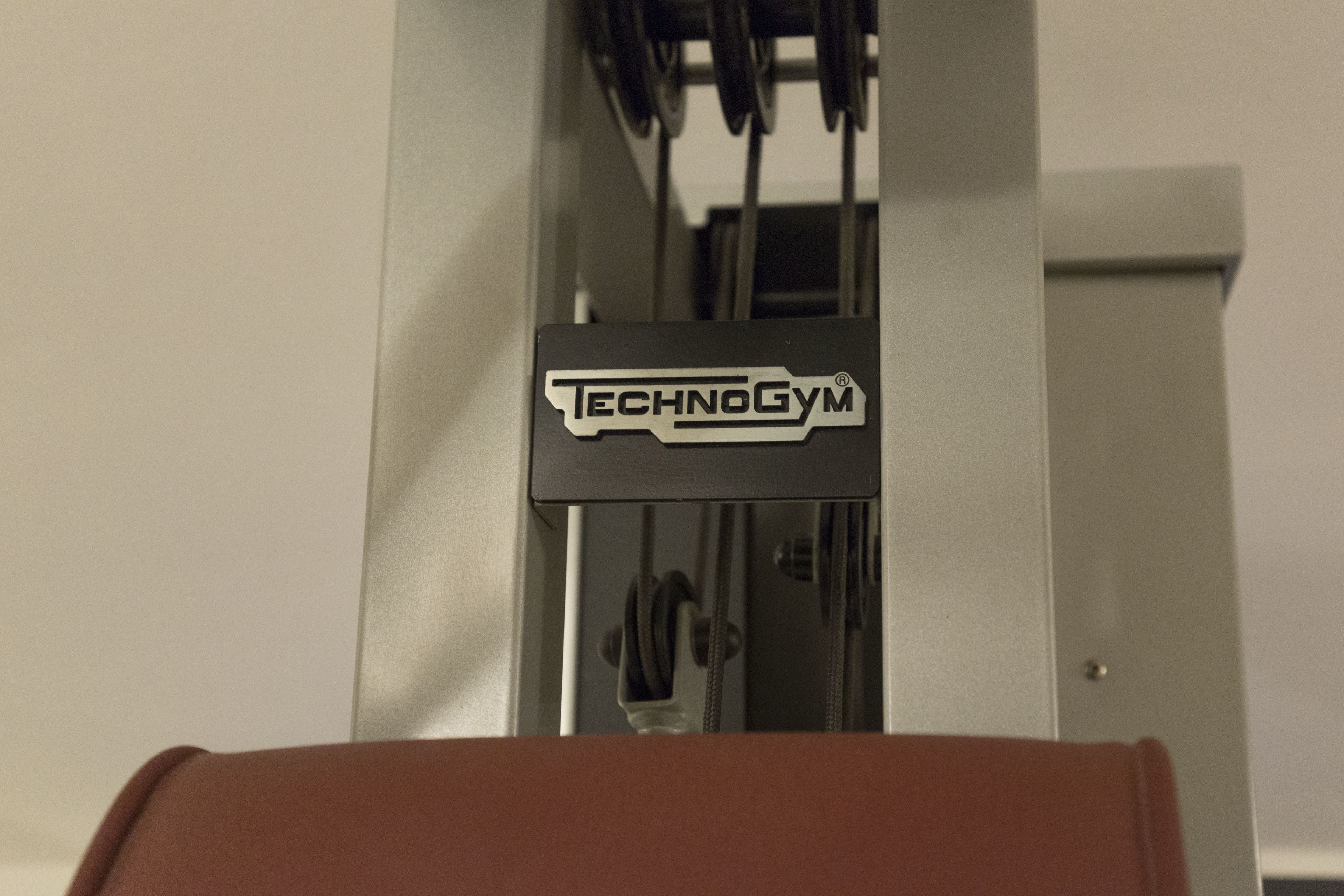 A gym equipment with the brand name "Technogym" visible on the machine.