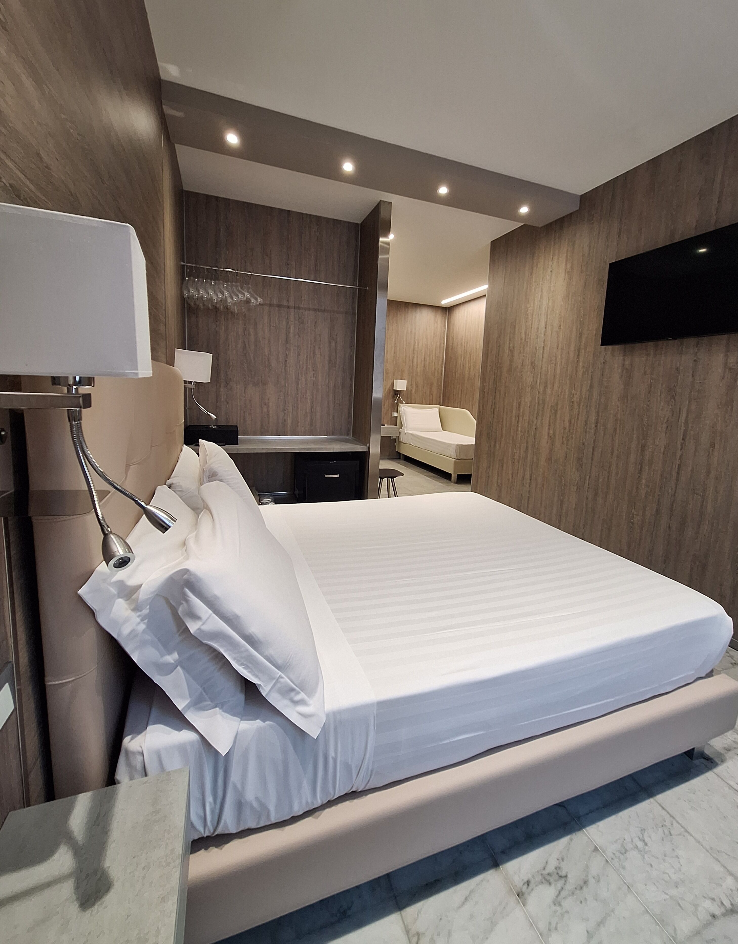 Una camera da letto moderna con un letto grande, un comodino, uno specchio e una TV a parete.