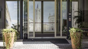 A hotel entrance with large glass doors, a view of a historic building, and potted plants on the sidewalk.
