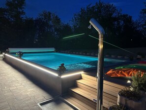 Una piscina con muelle de madera y estructura metálica, rodeada de árboles.
