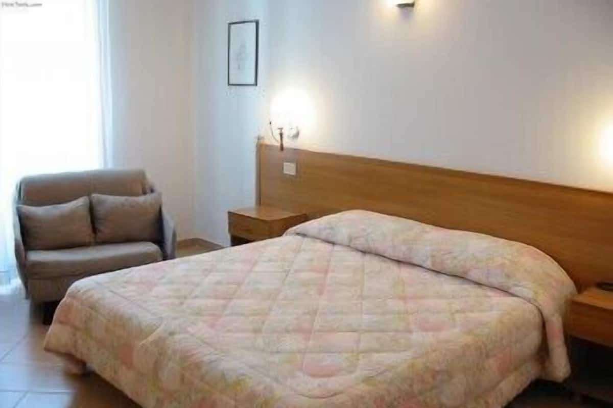 Un dormitorio con una cama, una mesita de noche, una silla y una lámpara fijada a la pared.