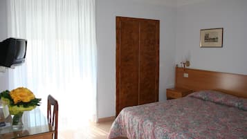 Habitación de hotel con cama, armario de madera, televisor sobre un mueble bajo y un cuadro enmarcado en la pared.