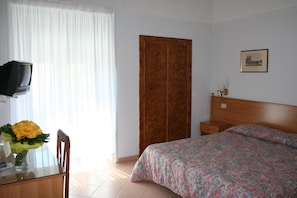 A hotel room with a bed, a wooden wardrobe, a television on a stand, and a framed picture on the wall. - Hotel Castello (Mesagne)