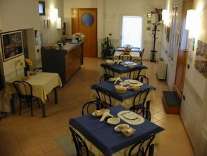 A dining area with tables set for a meal, a kitchen area with a refrigerator and counter, and a door leading to another room. - Hotel Castello (Mesagne)