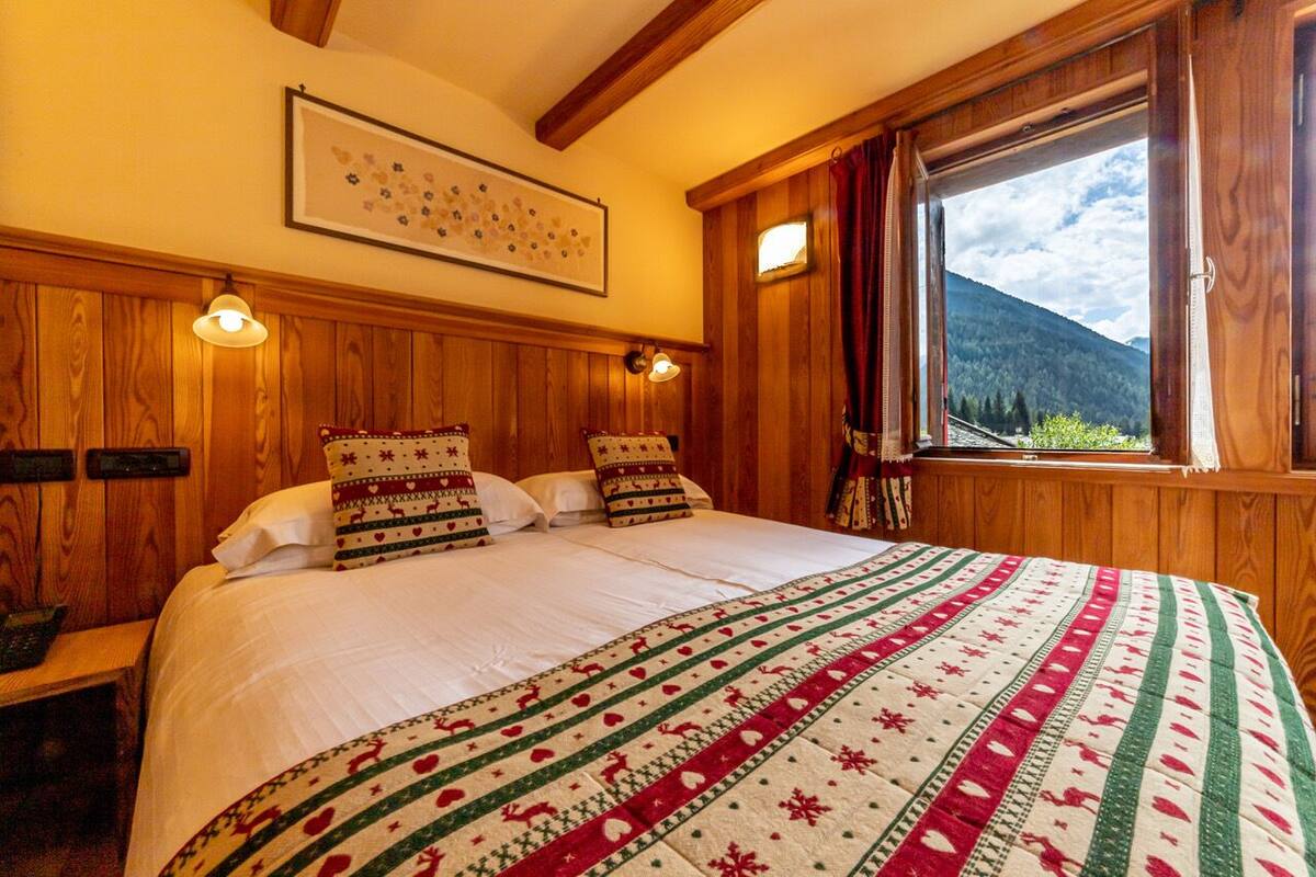 Una habitación acogedora de madera con una cama grande, una ventana con vistas a la montaña y un cuadro enmarcado en la pared.