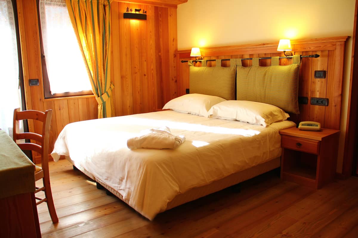 Una habitación de madera con cama, mesita de noche, silla y ventana con cortinas.