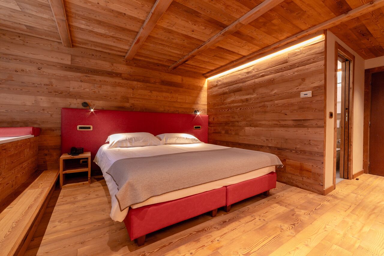 Una habitación con paneles de madera, una cama, una mesita de noche y un cabecero rojo.