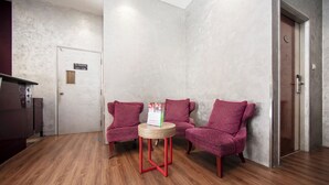 A reception area with a wooden floor, two pink patterned chairs, a small round table with a magazine, and a door labeled "101-106". - Fragrance Hotel - Rose (Singapore)