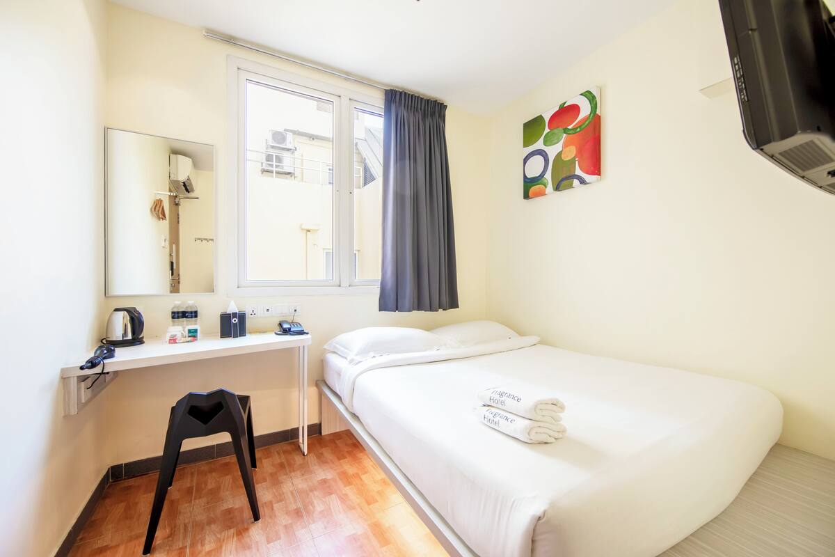 Une chambre d’hôtel comprenant un lit, un bureau, une chaise, une fenêtre avec des rideaux, un miroir et une œuvre d’art murale.