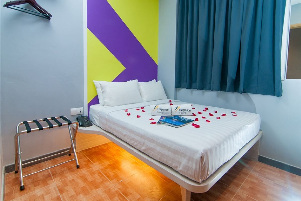 Una habitación de hotel con una cama, perchero y mesita de noche.