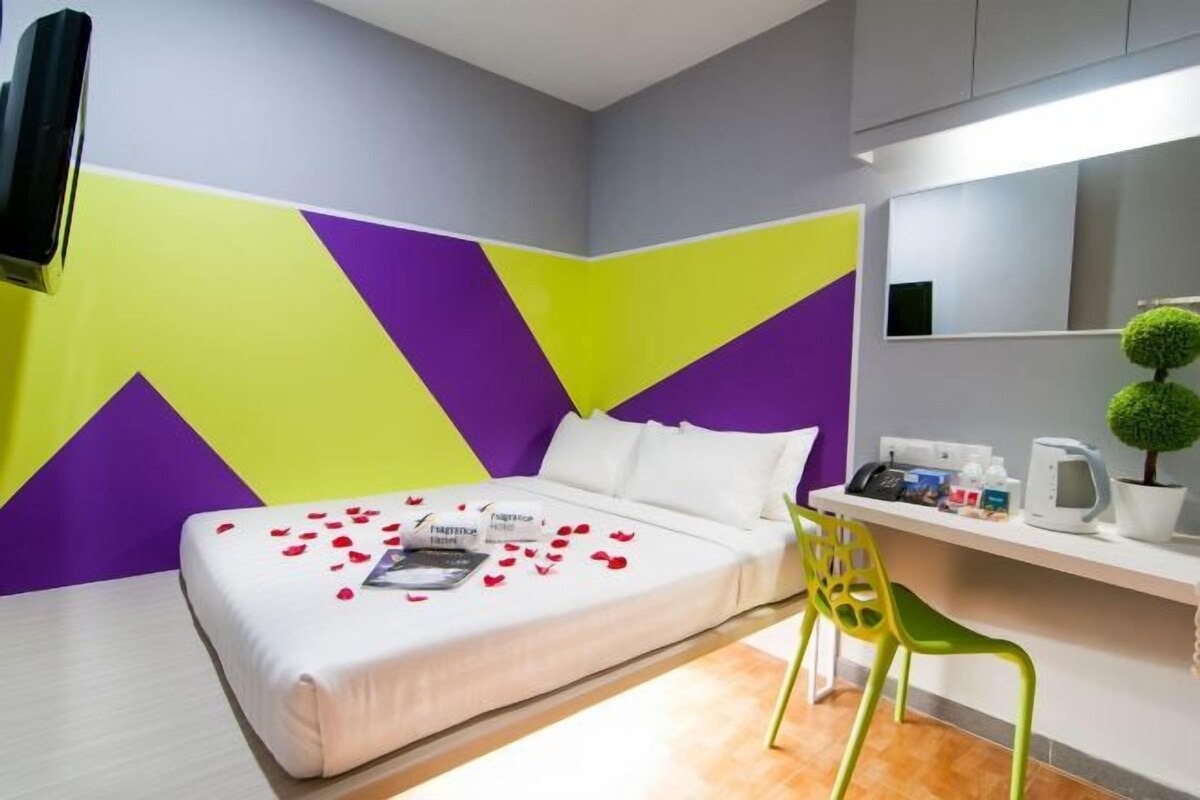 Habitación de hotel con cama, escritorio, silla, espejo y planta en maceta.