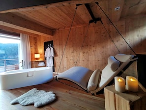 A wooden cabin interior with a hanging chair, a bathtub, and a view of the outdoors.