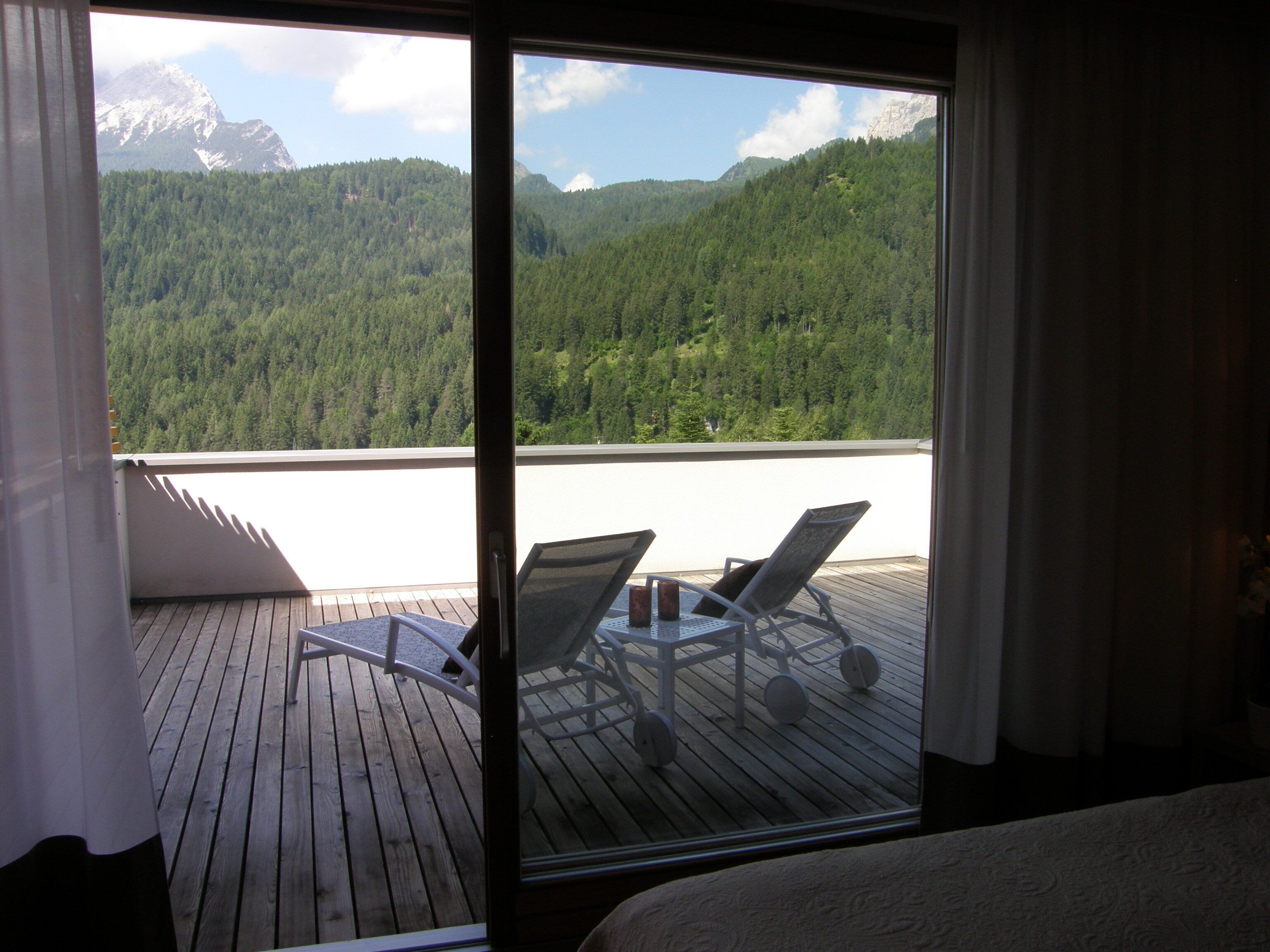 A balcony with two chairs and a table, overlooking a forested mountain range.