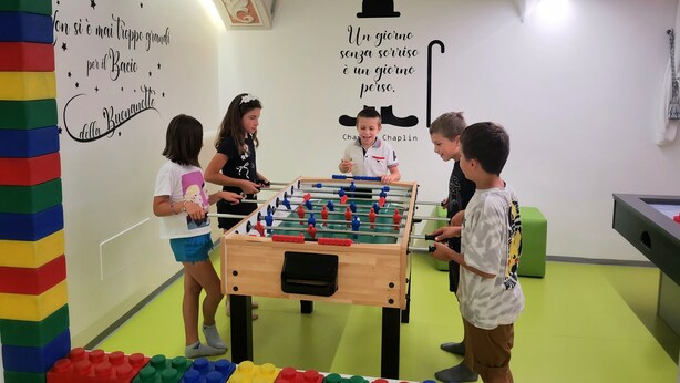 Een groep kinderen speelt tafelvoetbal in een helder verlichte kamer met kleurrijke wanden en een tafelvoetbaltafel.