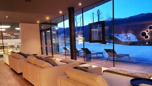 A modern interior with a sofa and chairs facing large windows overlooking a snowy landscape.