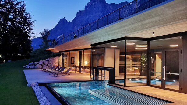 A modern house with a swimming pool, lounge chairs, and a stone wall.