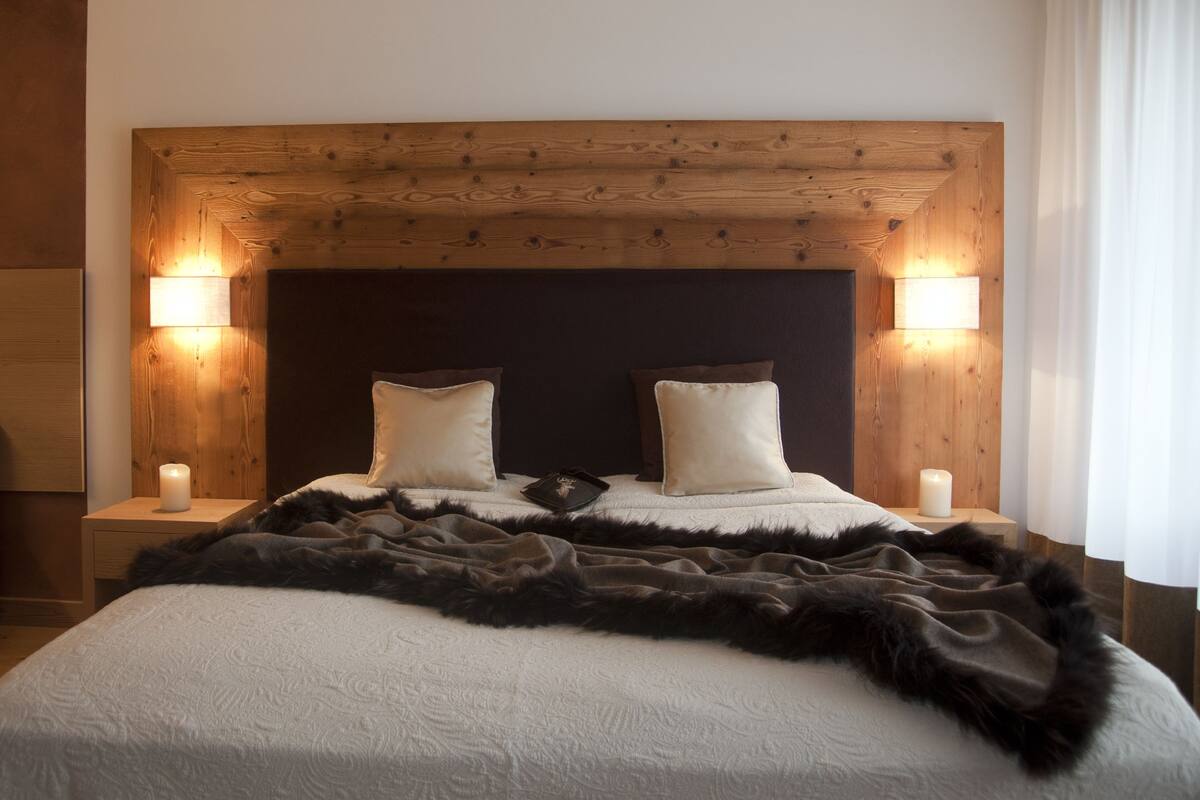 Une chambre à coucher avec une tête de lit en bois, deux lampes de chevet, un lit recouvert d’une couverture noire et blanche, et deux oreillers blancs.