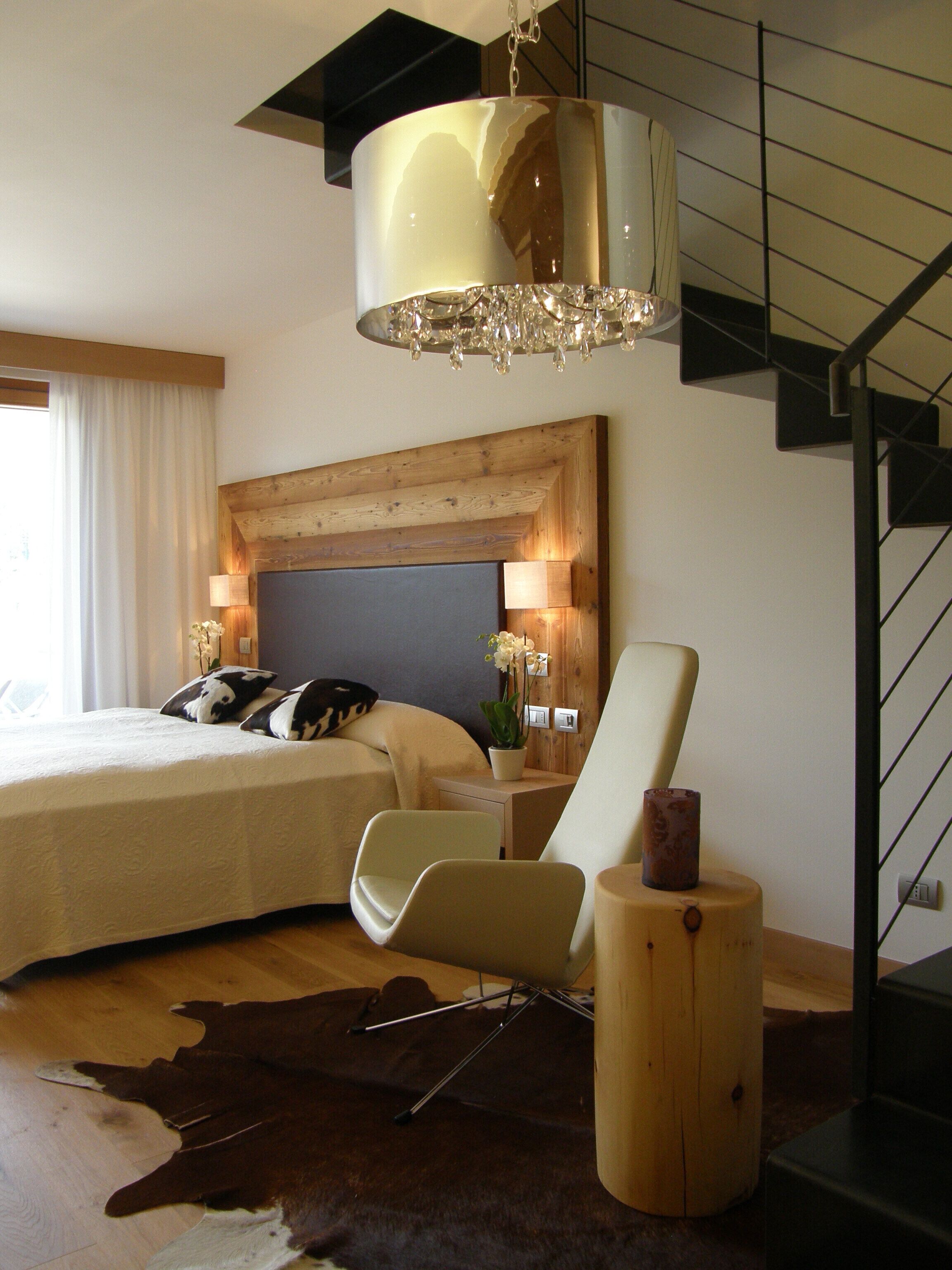 Ein modernes Schlafzimmer mit einem großen Bett, einem Holzkopfteil, einer Chandelüster, einem Schreibtisch mit Lampe und einer Treppe.