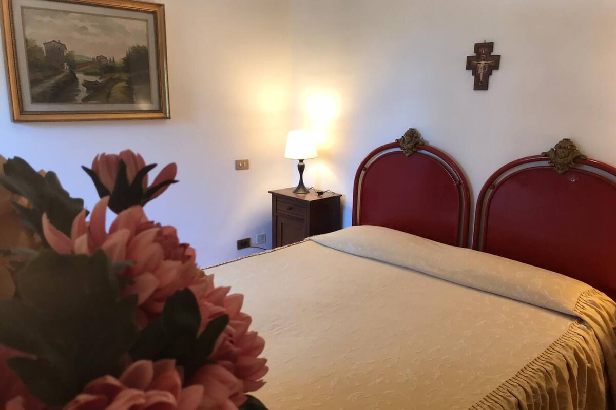 Une chambre à coucher avec un lit, une table de chevet avec une lampe, un tableau encadré et une croix accrochée au mur.