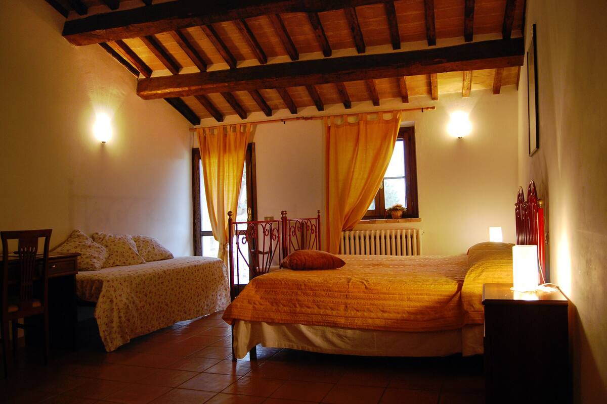 Une chambre avec deux lits, un plafond en bois, un radiateur et une fenêtre avec des rideaux.