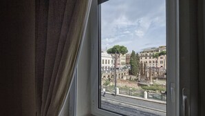 A window with a view of ancient ruins and a tree. - Little Queen Suite (Rome)