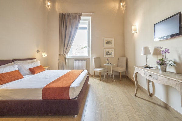 A hotel room with a large bed, a desk, a chair, a TV, and a window with curtains.