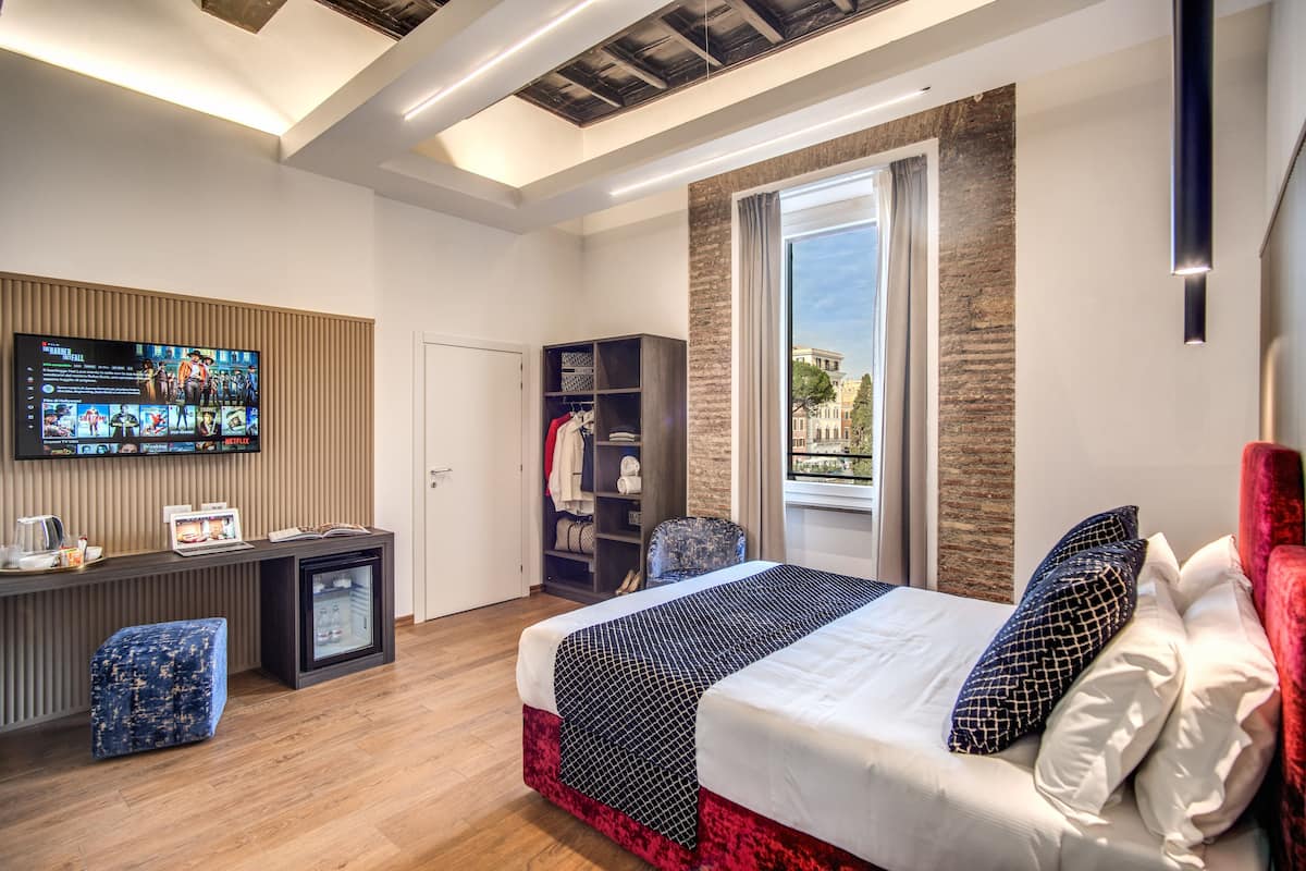 Ein modernes Hotelzimmer mit einem großen Bett, einem an der Wand montierten Fernseher, einem kleinen Schreibtisch mit einem Laptop und einem Kleiderschrank.