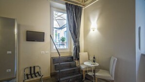 A hotel room with a staircase, a flat-screen TV, a small table with a chair, and a window with curtains. - Little Queen Suite (Rome)