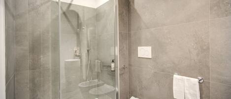 Un baño moderno con ducha envuelta en vidrio, inodoro blanco y lavamanos con espejo.