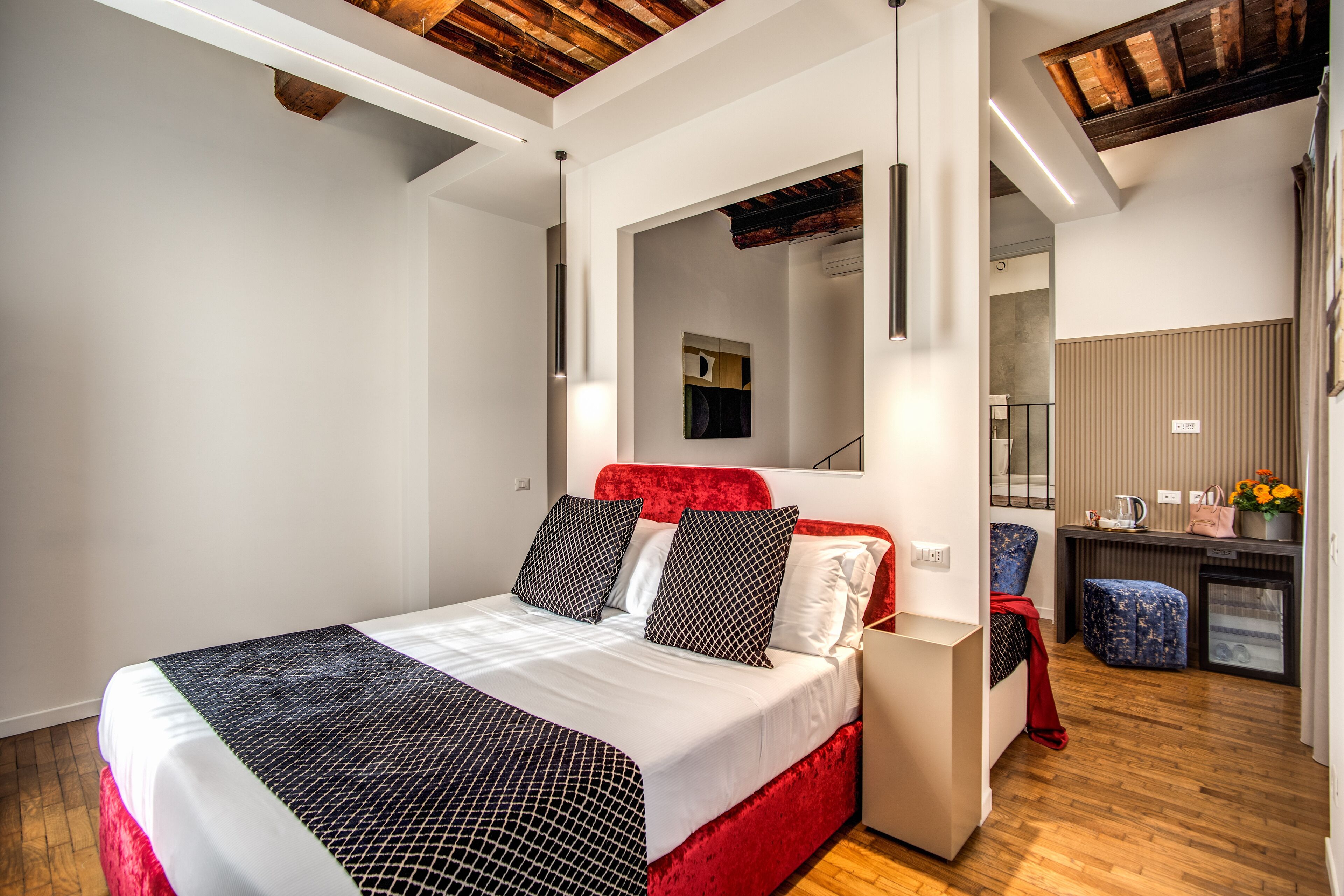 A modern bedroom with a red bed, white bedding, and a wooden ceiling.