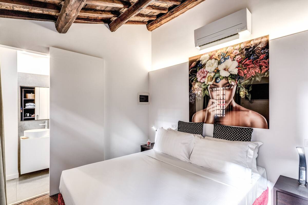 Ein Schlafzimmer mit einem großen Bett, einem Nachttisch, einer Wand-Klimaanlage und einem durch eine offene Tür einsehbaren Badezimmer.