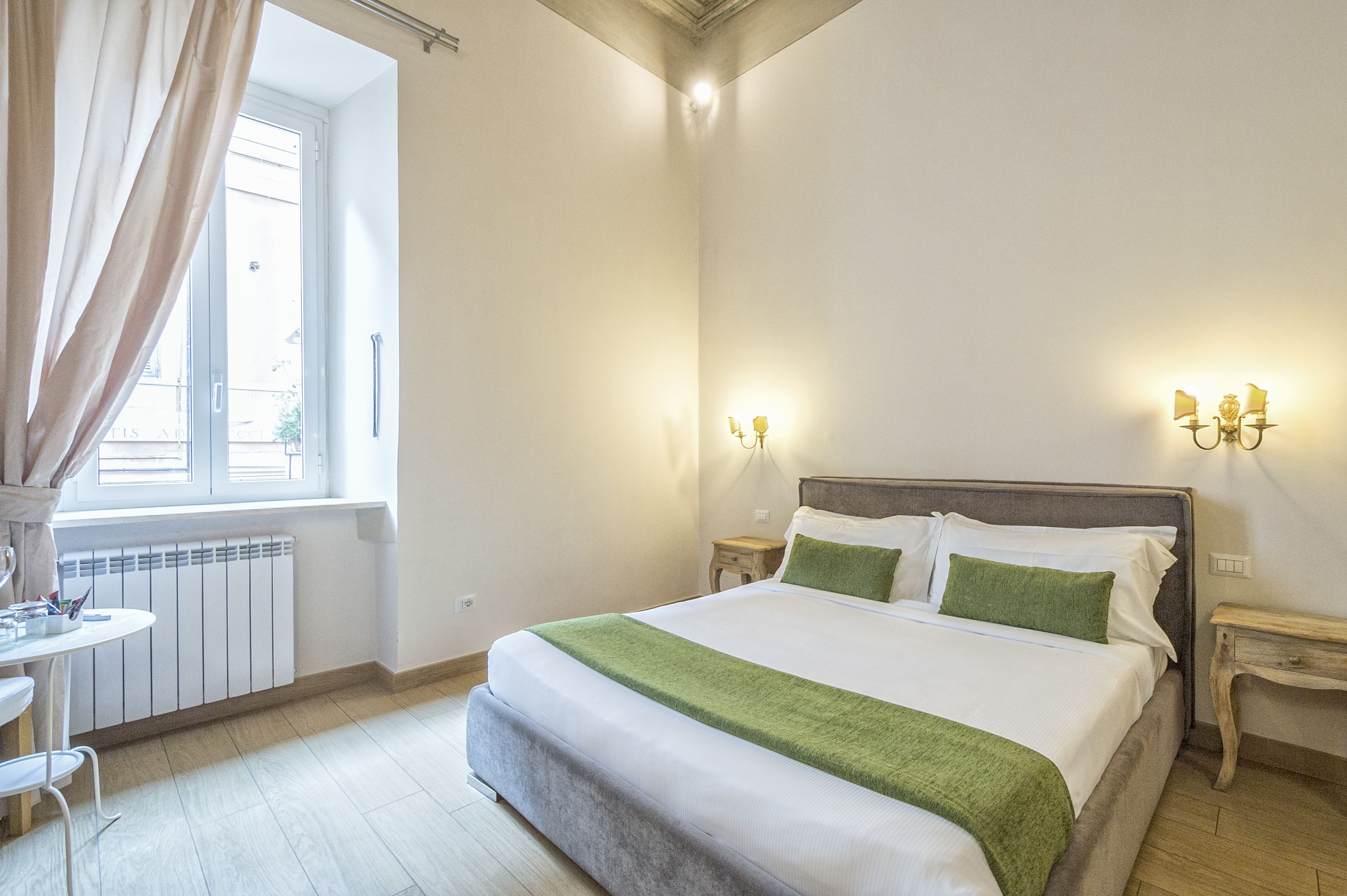 Une chambre bien rangée, avec un grand lit, des tables de chevet, une fenêtre avec des rideaux et un radiateur.