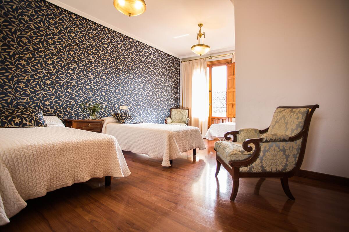 A hotel room with two beds, a chair, a nightstand, and a window with curtains.