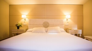 Una habitación de hotel con una cama grande, dos lámparas de noche, una mesita de noche con un teléfono y una pequeña planta en maceta.