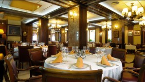 Un comedor formal con mesas redondas dispuestas para el servicio, sillas de madera y candelabros.